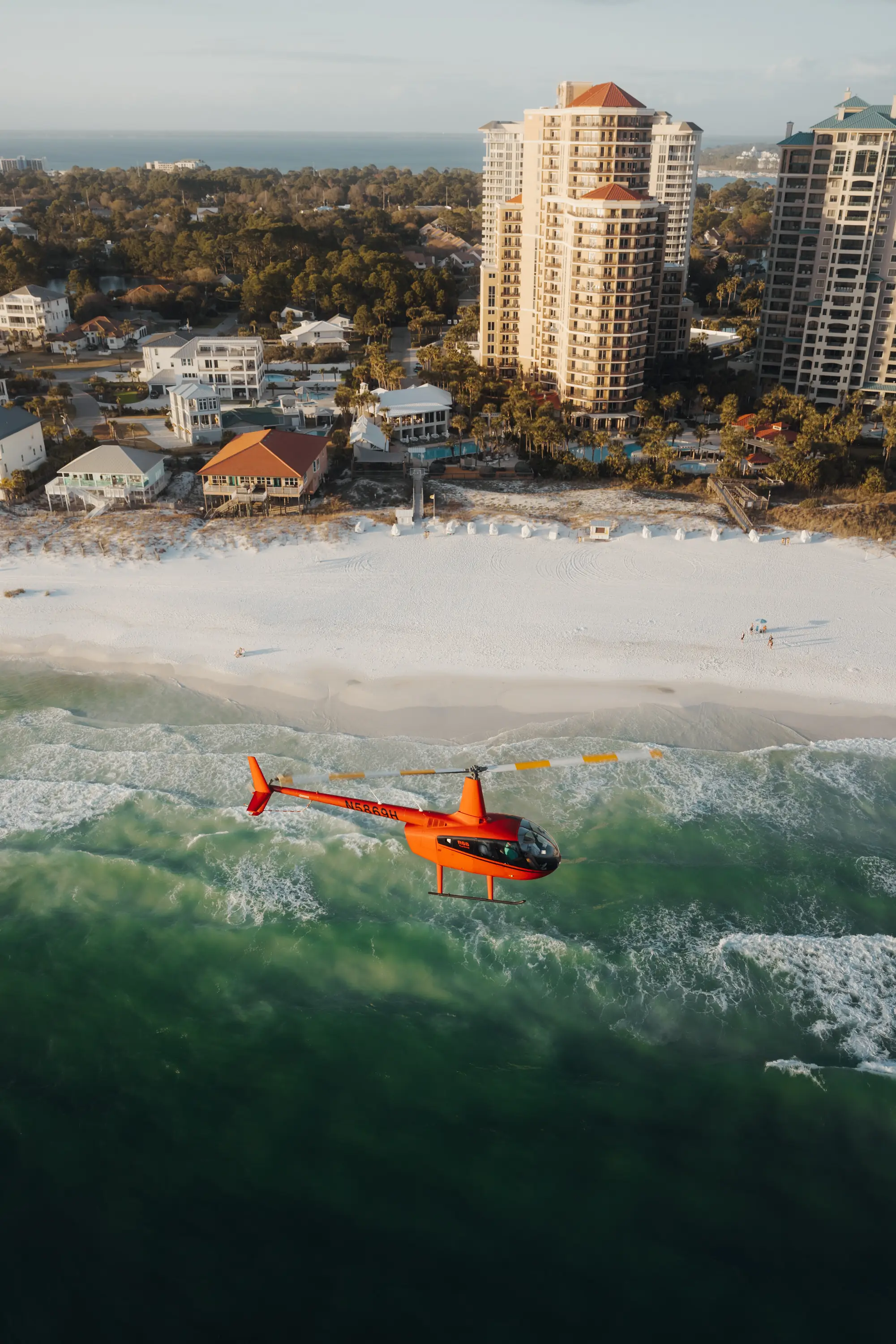 Aerial of a red helicopter over the Gulf near beachfront high-rises