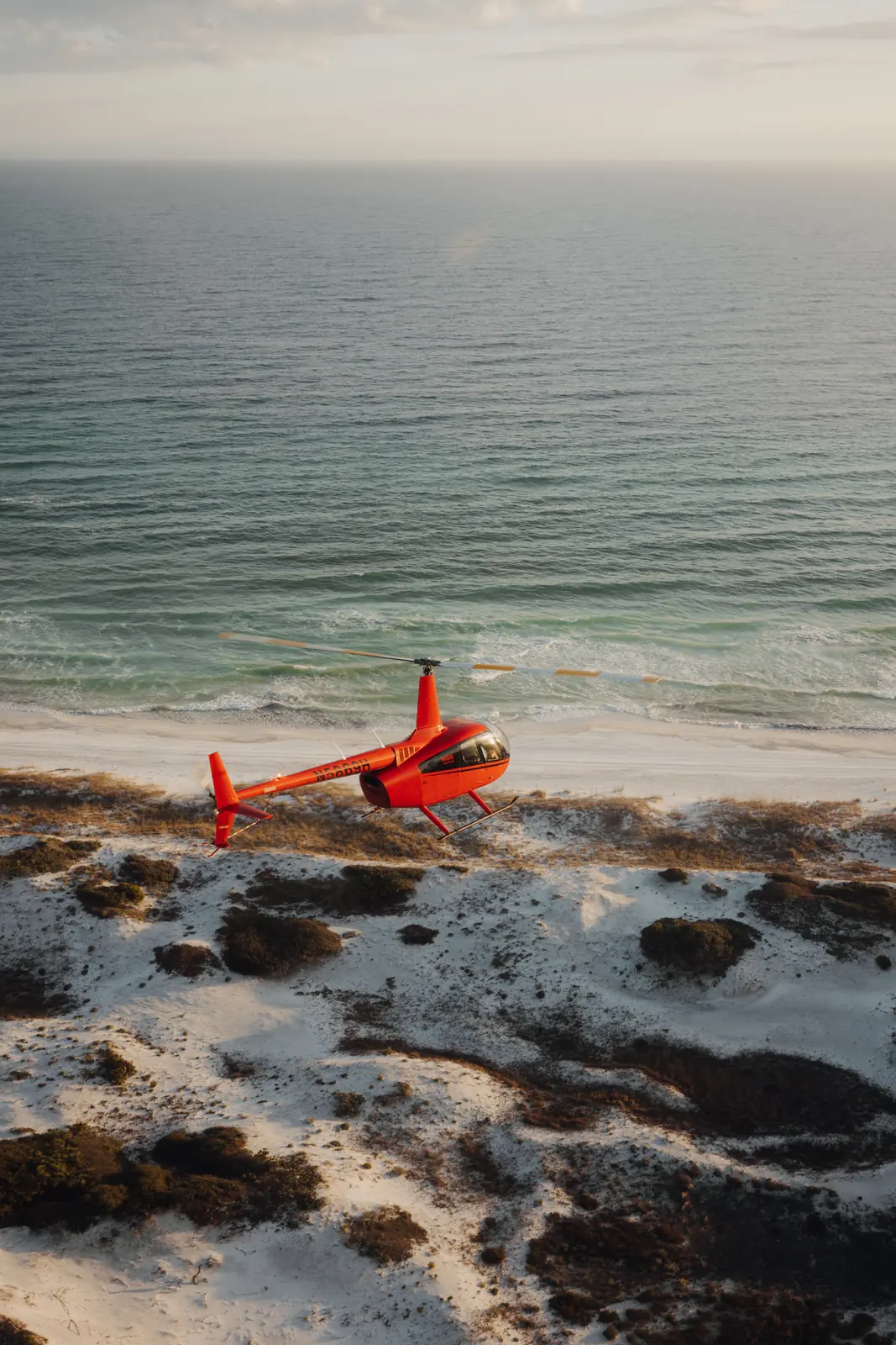 Aerial of a helicopter over white sand and the Gulf