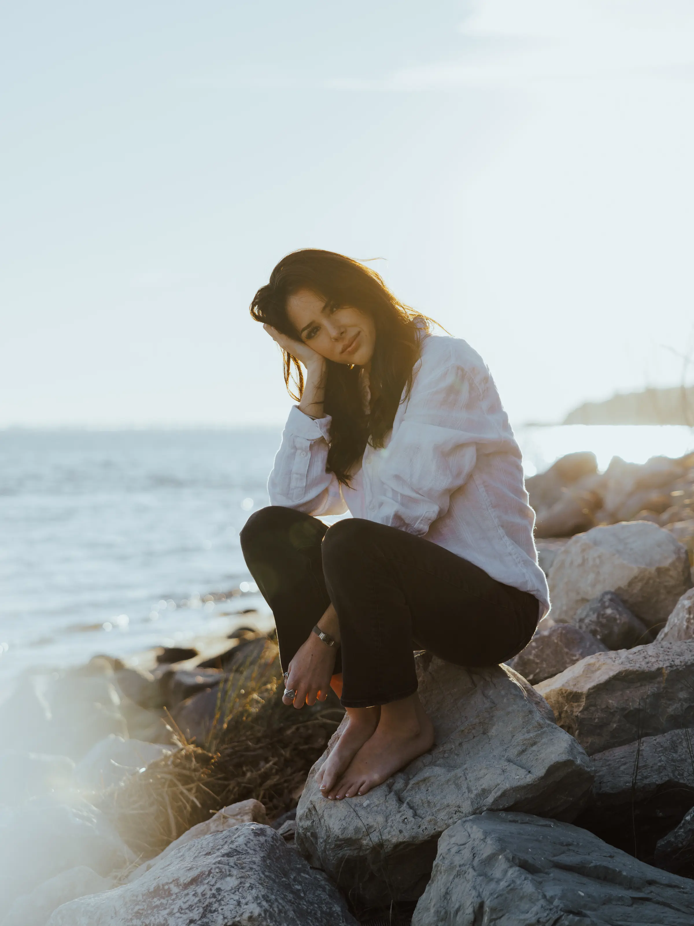 Woman sitting on jetty rocks by the water, laughing