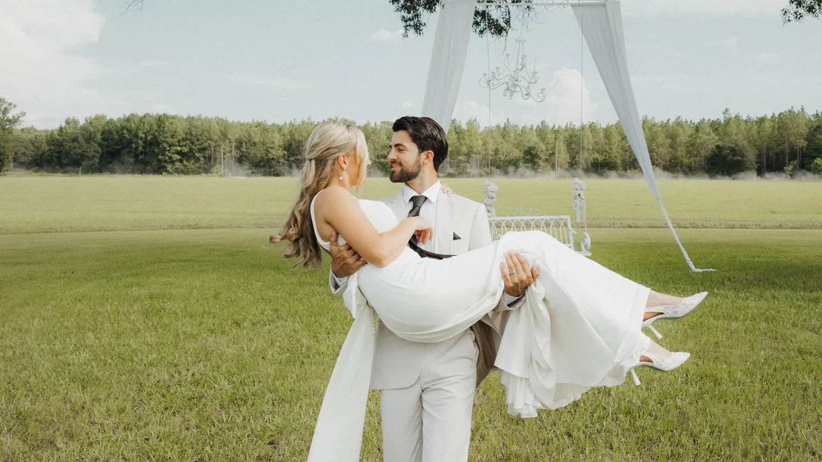 Groom carrying the bride across a green field
