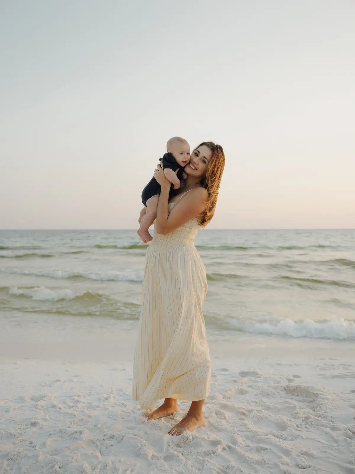 Mother lifting her child at the water's edge at dusk