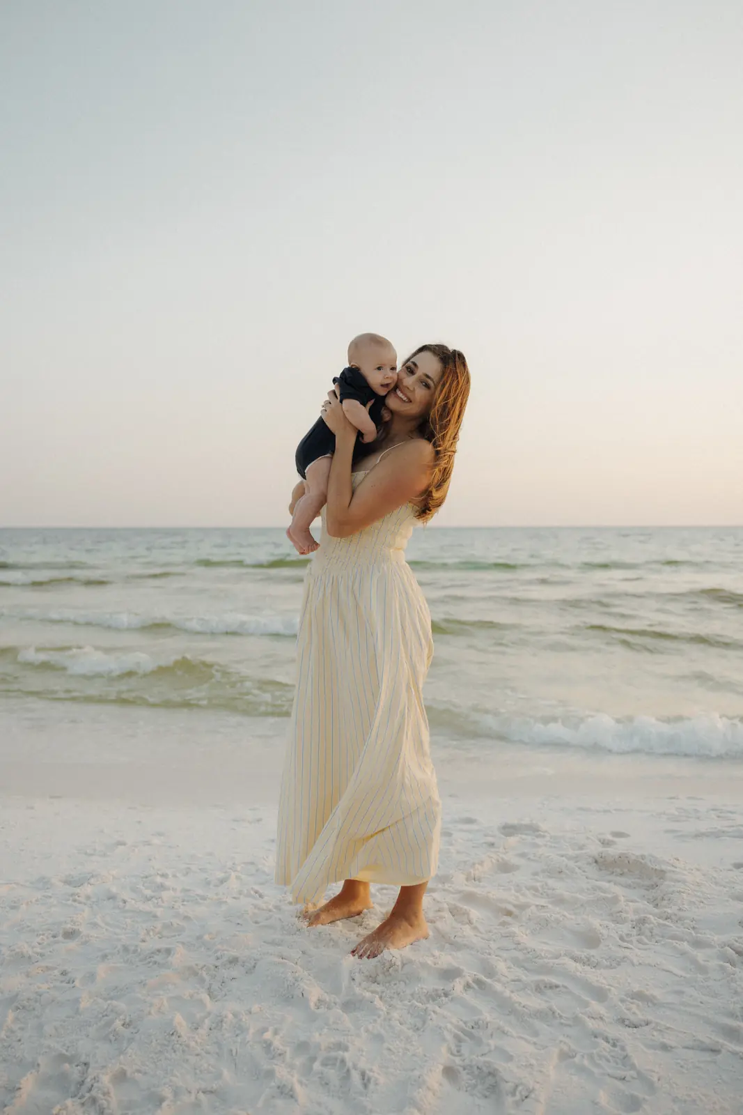 Mother holding her toddler at the shoreline at golden hour