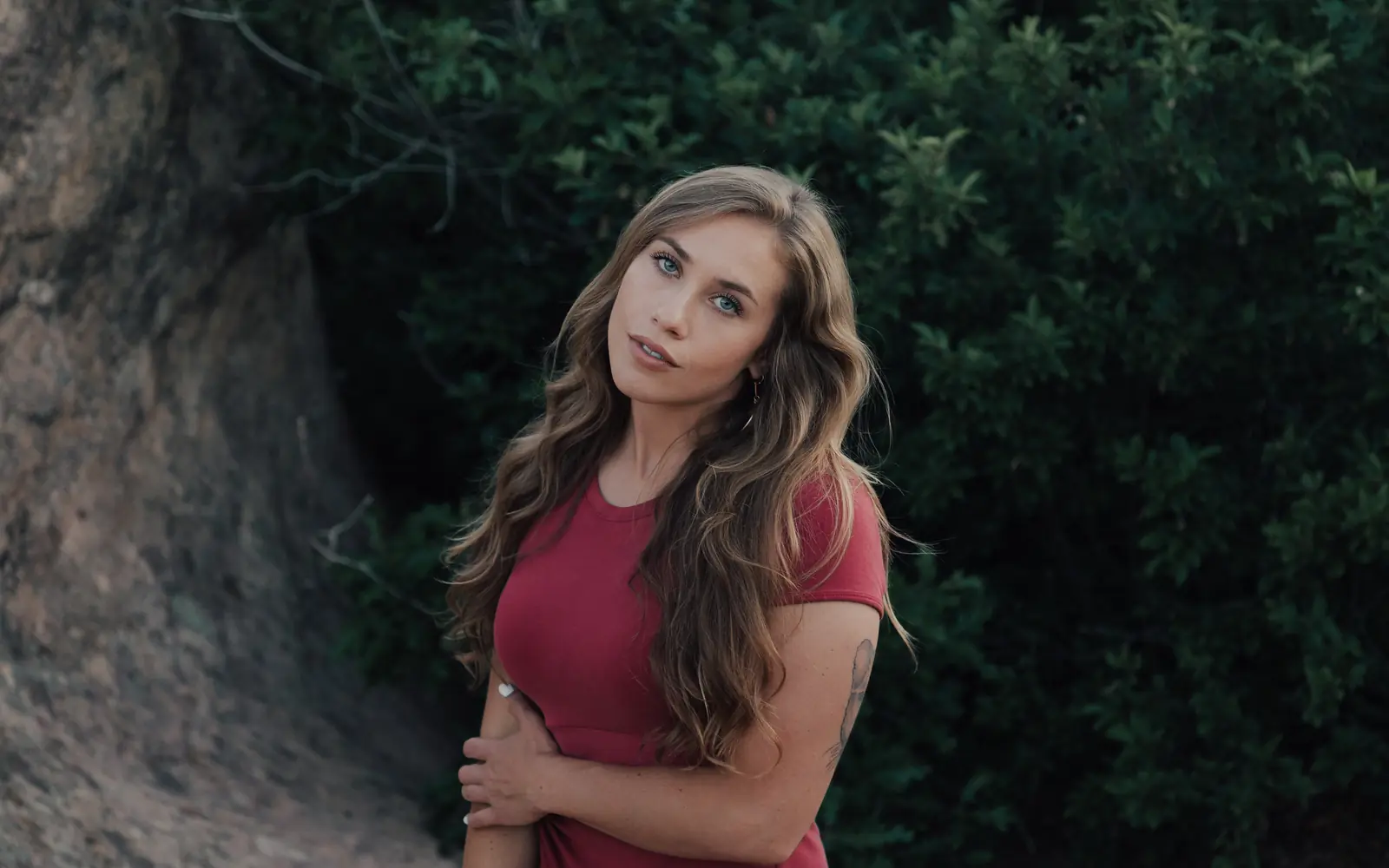 Woman in a red top posing against dark greenery