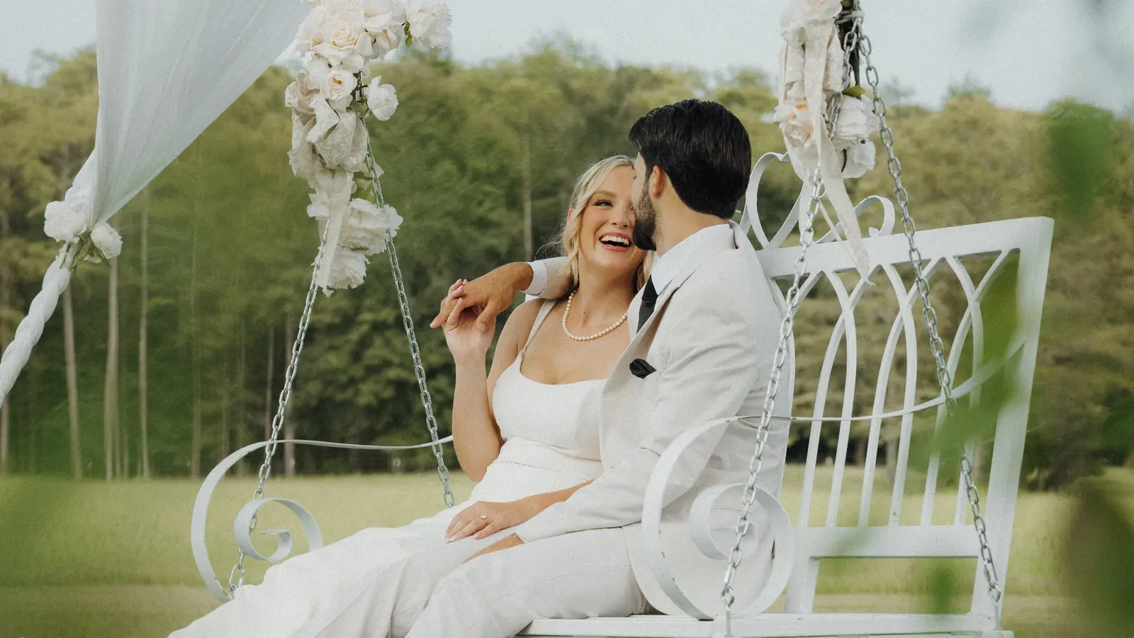 Bride and groom laughing on a white garden swing