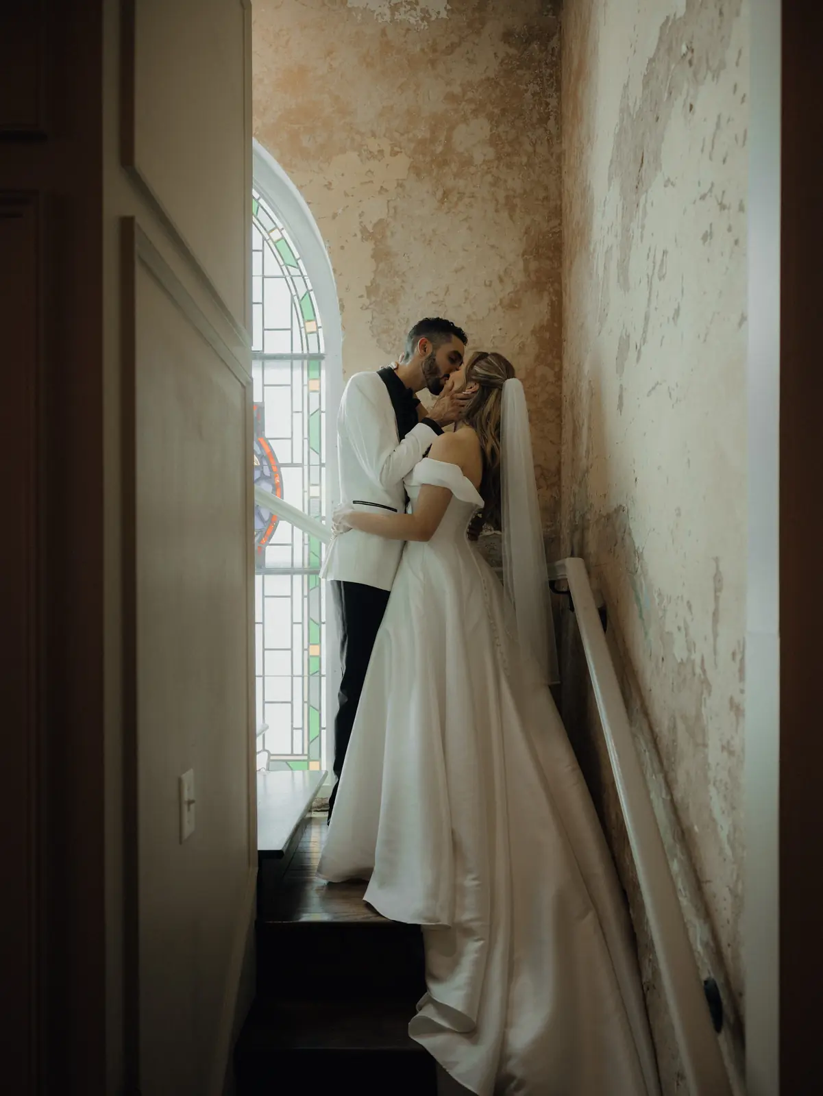 Bride and groom kissing in a sunlit historic stairwell