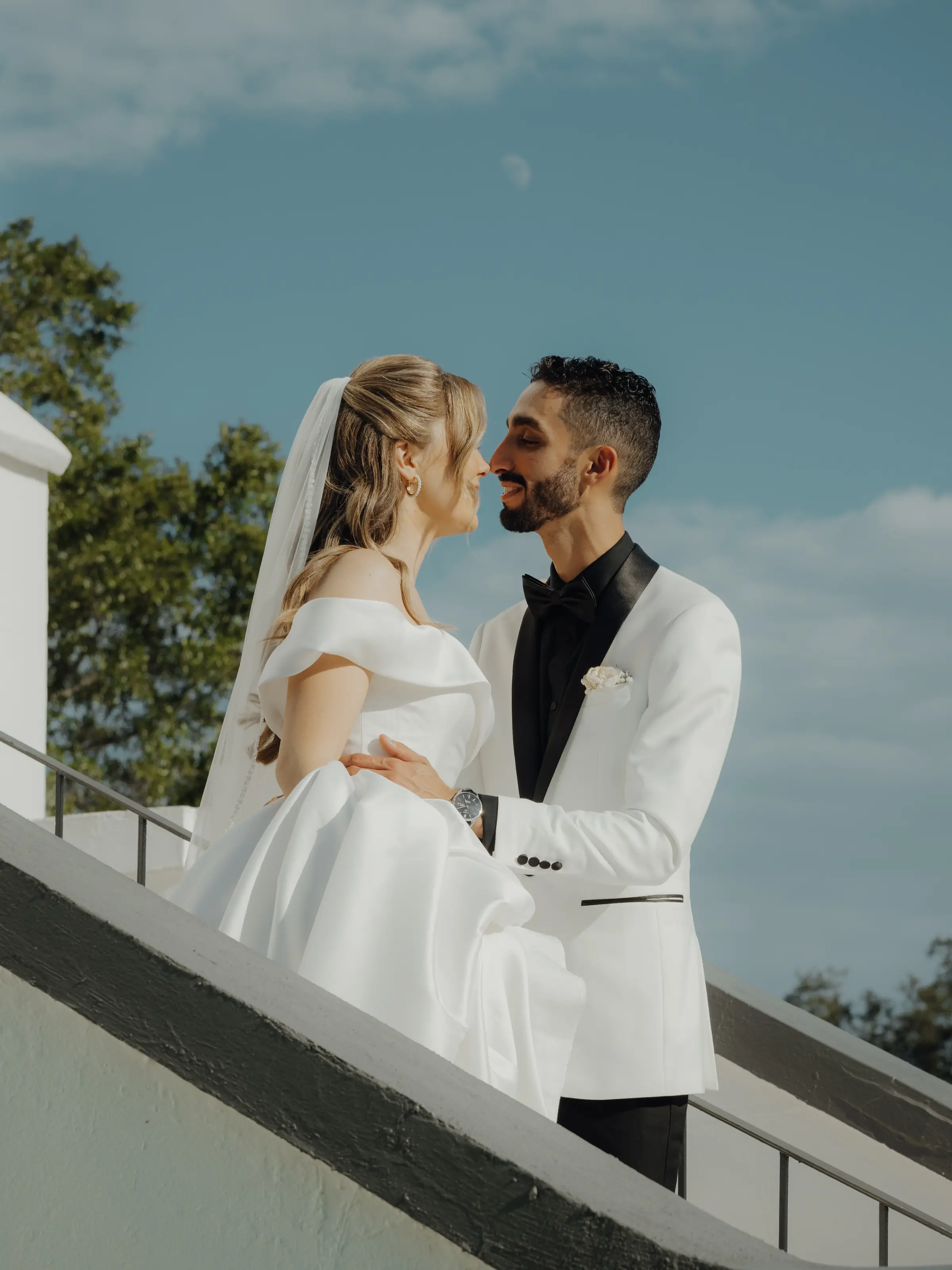 Bride and groom on white chapel steps under blue sky